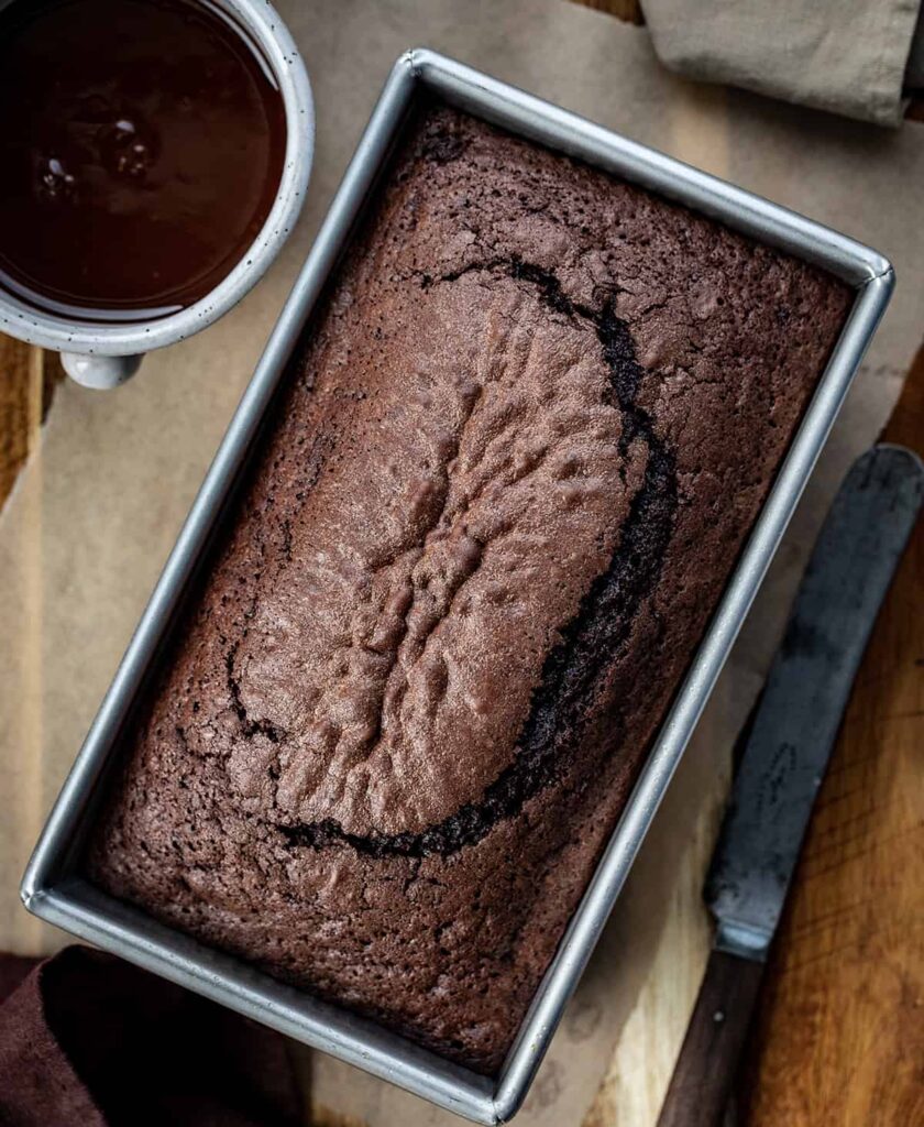 El pan de brownie es una hogaza de pan de chocolate con textura suave, similar a un brownie, pero cortada y servida como una rebanada de pan. Además, el ganache de chocolate con leche le da aún más sabor a chocolate. ¡Es un pan rápido que seguro se acabará enseguida! Este delicioso postre satisfará tu gusto por lo dulce y tu antojo de chocolate.